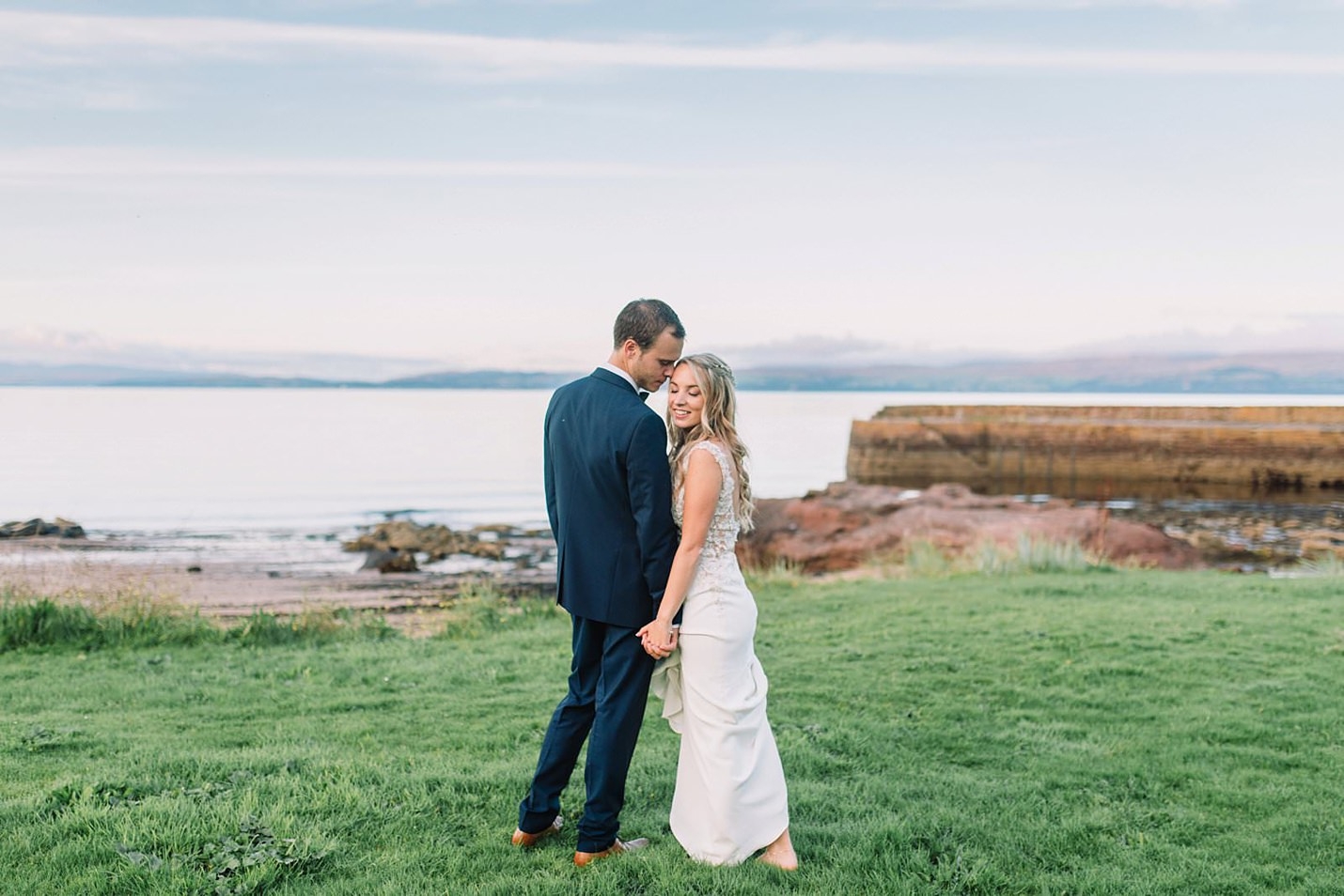 bride and groom pose in front of a loch with hills in the background Wedding Photographer Scotland The Gibsons