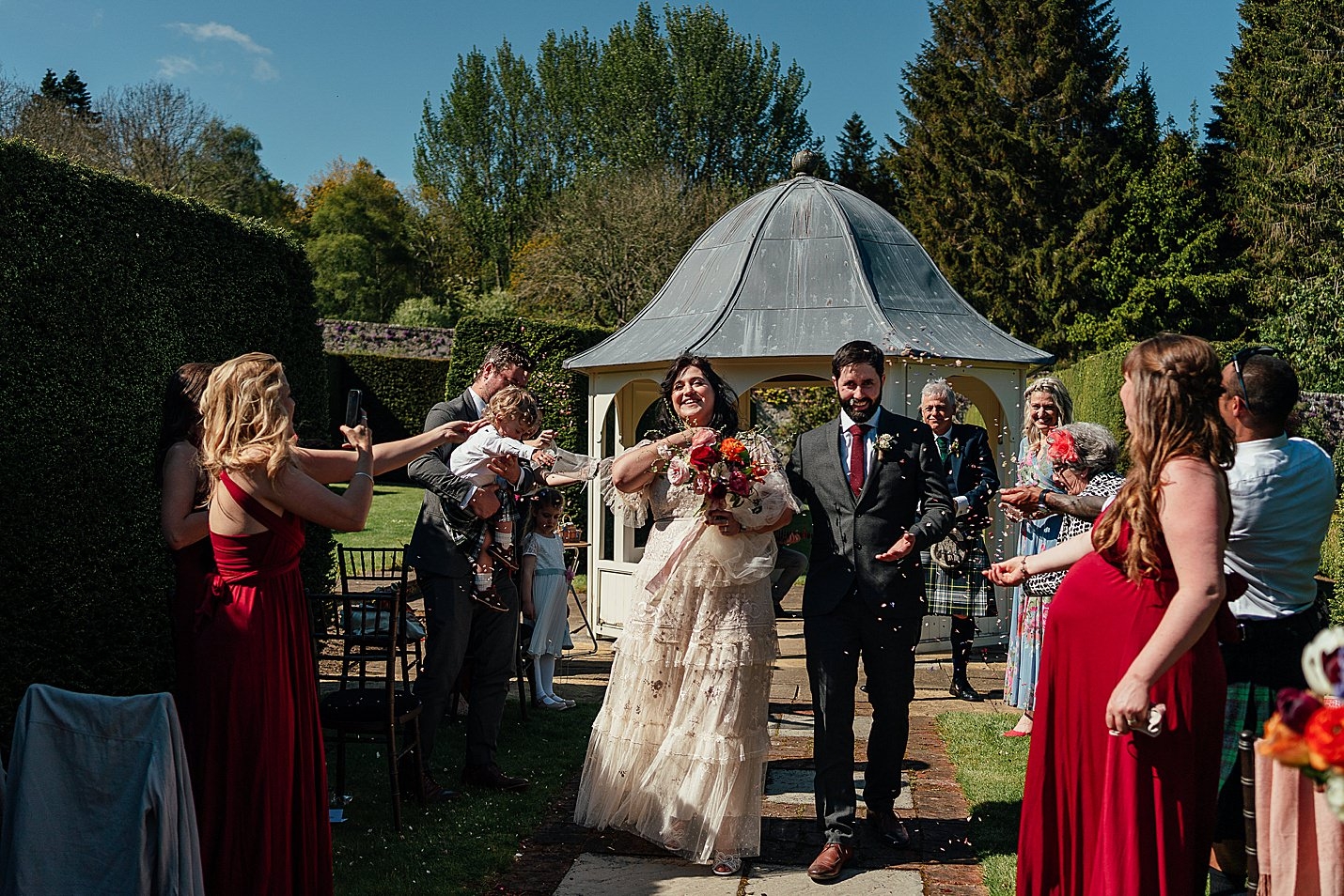 mariés juste mariés marchant dans l'allée dans un jardin clos avec des invités jetant des confettis château de tambour mariage fotomaki photographie