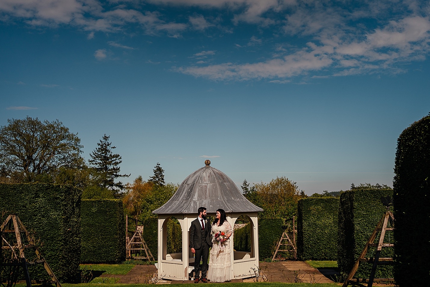 Les mariés qui viennent de se marier se regardent dans les yeux dans un jardin clos avec des haies vertes le jour ensoleillé du château de tambour photographie fotomaki de mariage