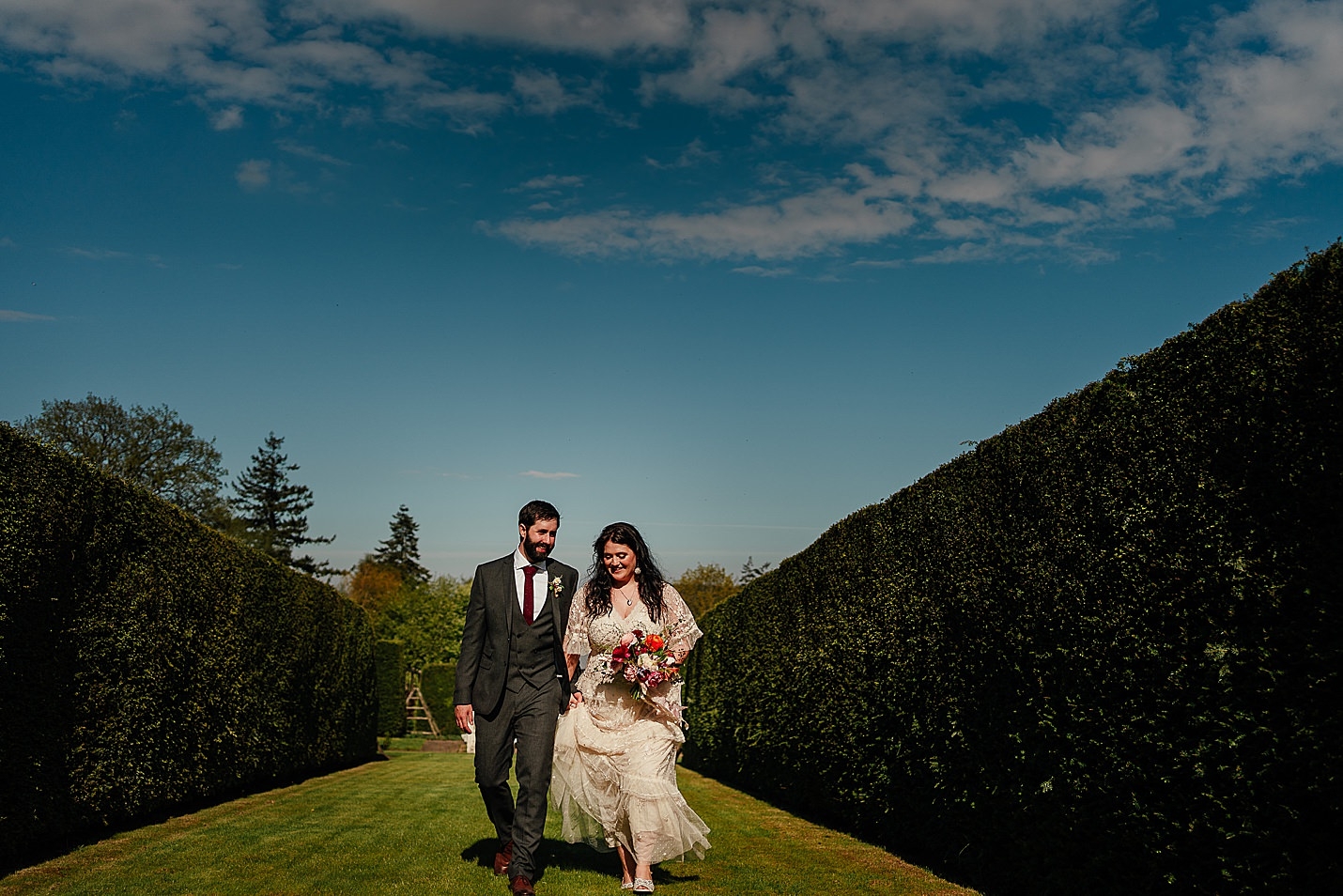Les mariés viennent de se marier marchant vers la caméra dans un jardin clos vert avec un ciel bleu le jour ensoleillé château de tambour photographie fotomaki de mariage