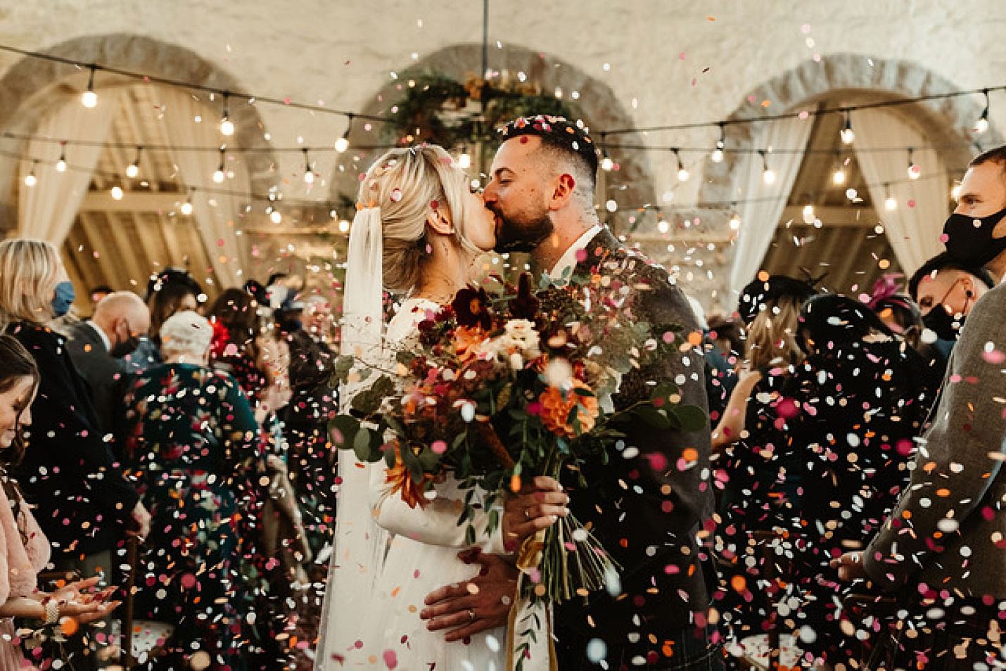 photo de la mariée et du marié s'embrassant alors que les invités au mariage jettent des confettis la mariée tient un superbe bouquet de mariée par gloam emma lawson photographie