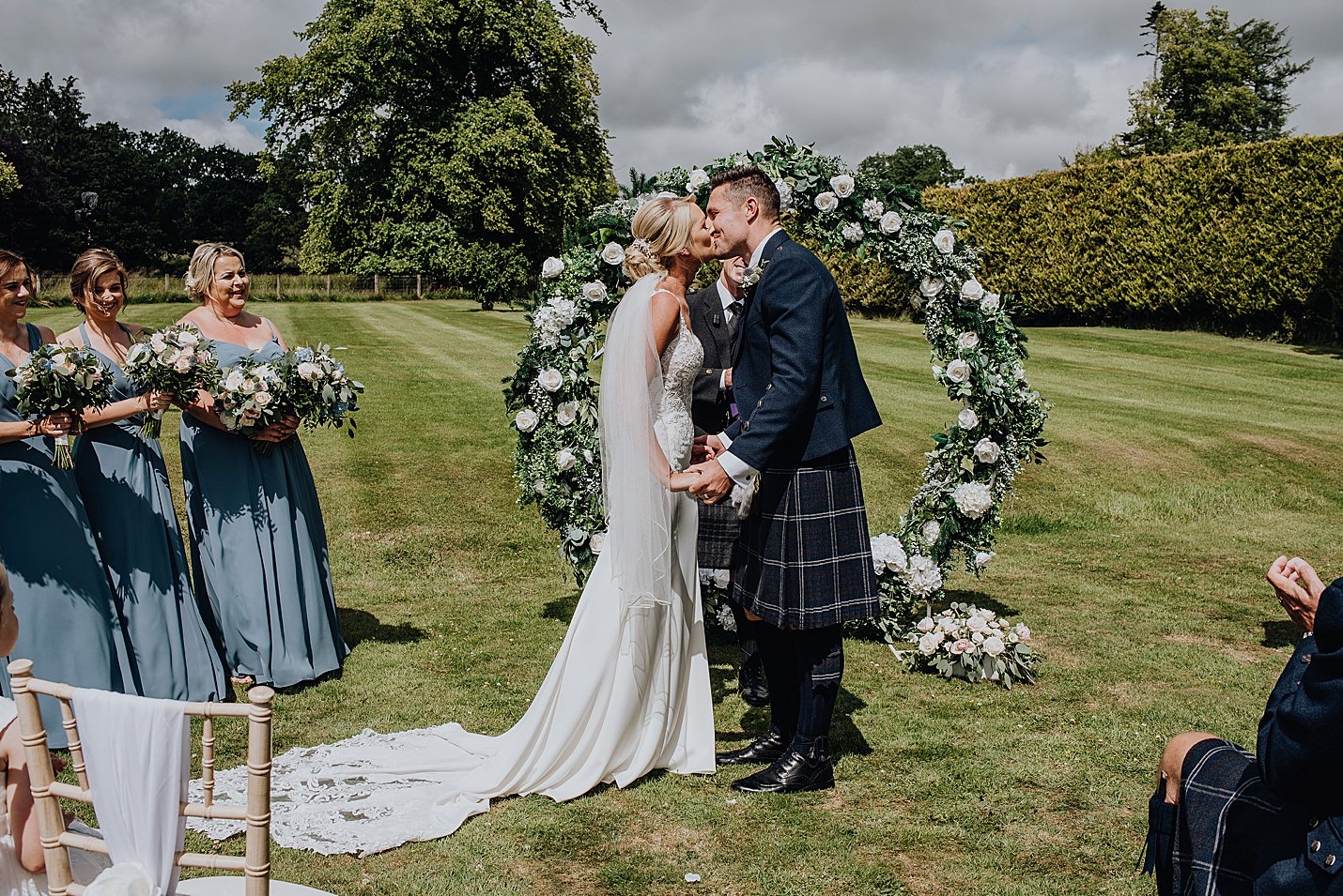 bride and groom first kiss at ceremony in front of floral arch on grass lawn sorn castle wedding