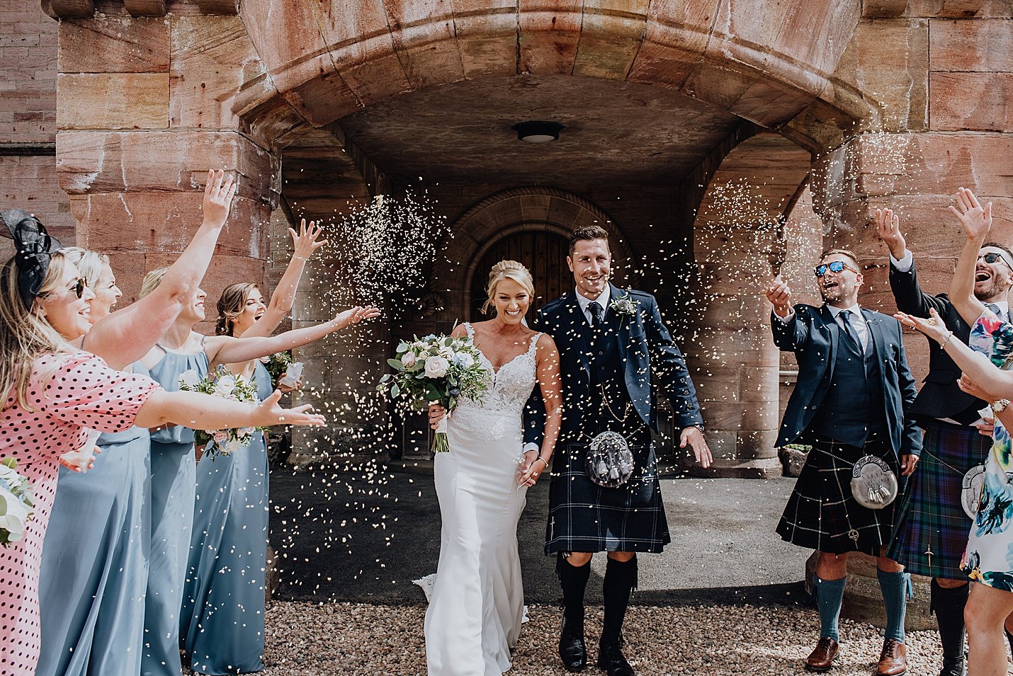 bride and groom walking out of castle as guests shower them in confetti martin vernham photography