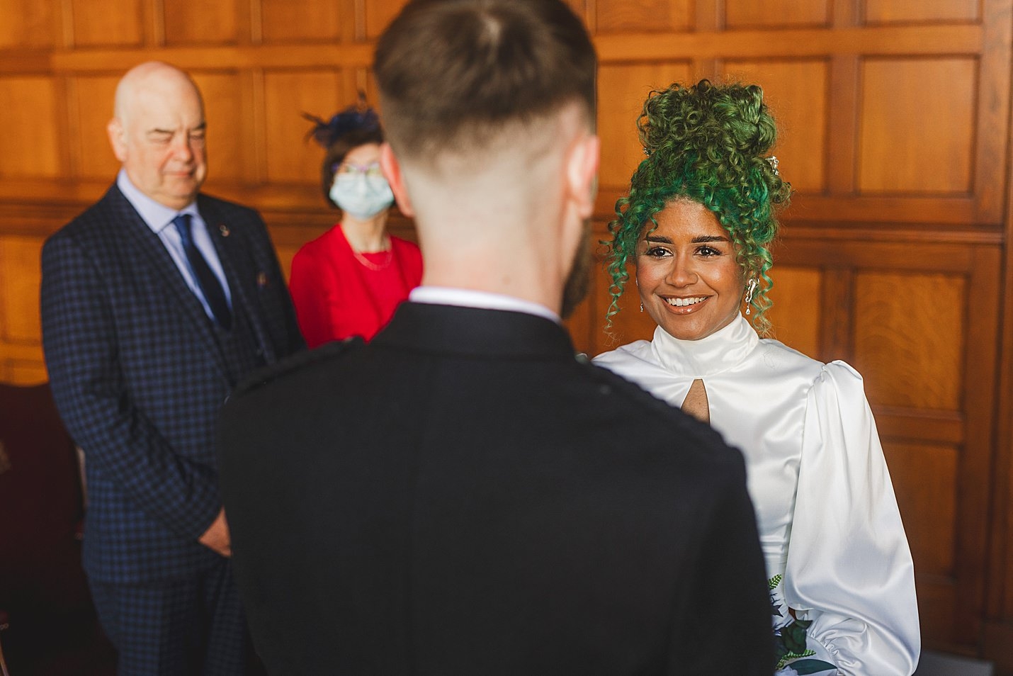 view from behind groom of bride wearing white dress with green hair smiling at ceremony marischal college wedding clarke joss photography