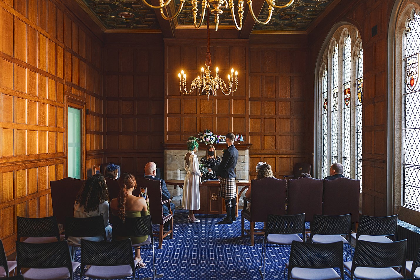 bride and groom look on as celebrant reads in ceremony room with wooden panel walls and arch windows marischal college wedding clarke joss photography