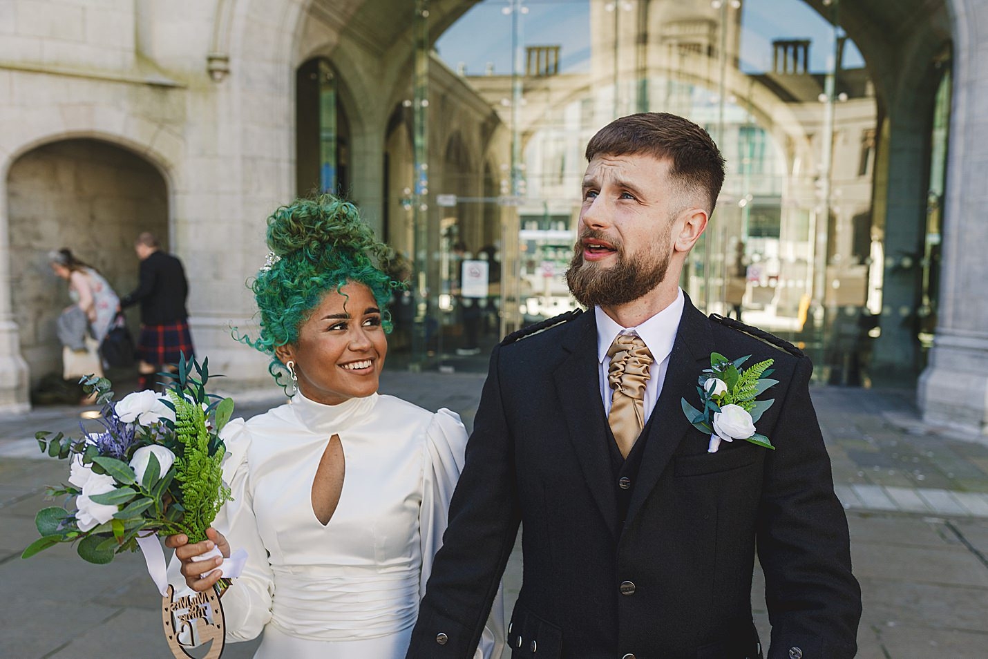 bride wearing white dress with green hair and groom wearing kilt outfit walking hand in hand as they leave the venue marischal college wedding clarke joss photography