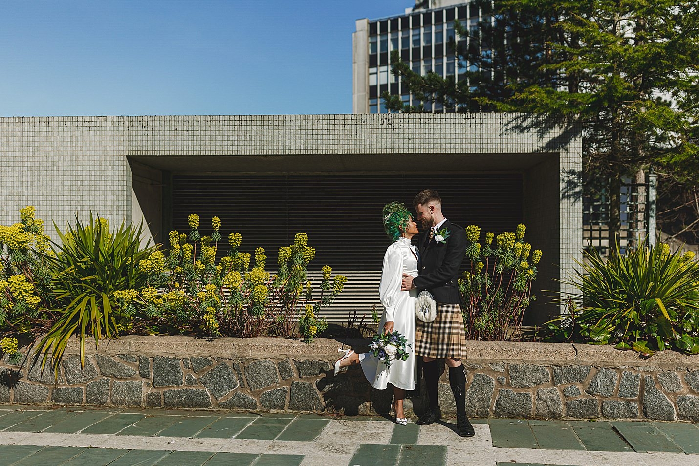 groom holds brides waist as they look into each others eyes tiled building wall and plants in background marischal college wedding clarke joss photography