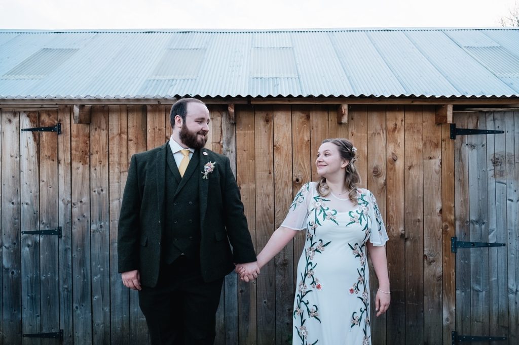 Bride wearing floral dress and groom in a tweed suit at their wedding at Comrie Croft, Perthshire, Scotland