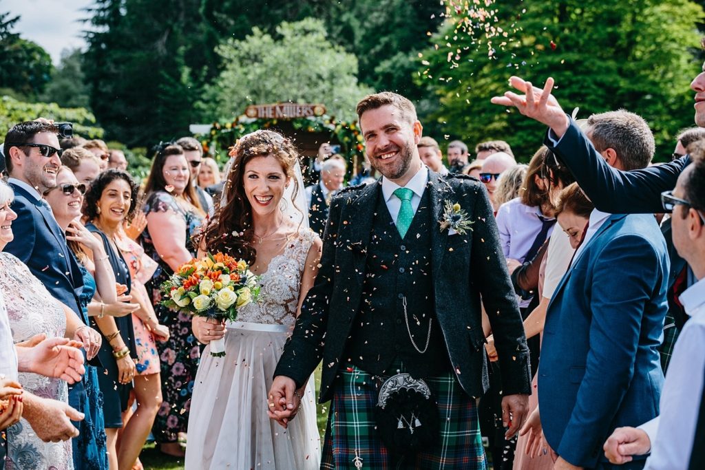 Bride and groom walk down aisle as confetti is thrown at their outdoor Scottish wedding
