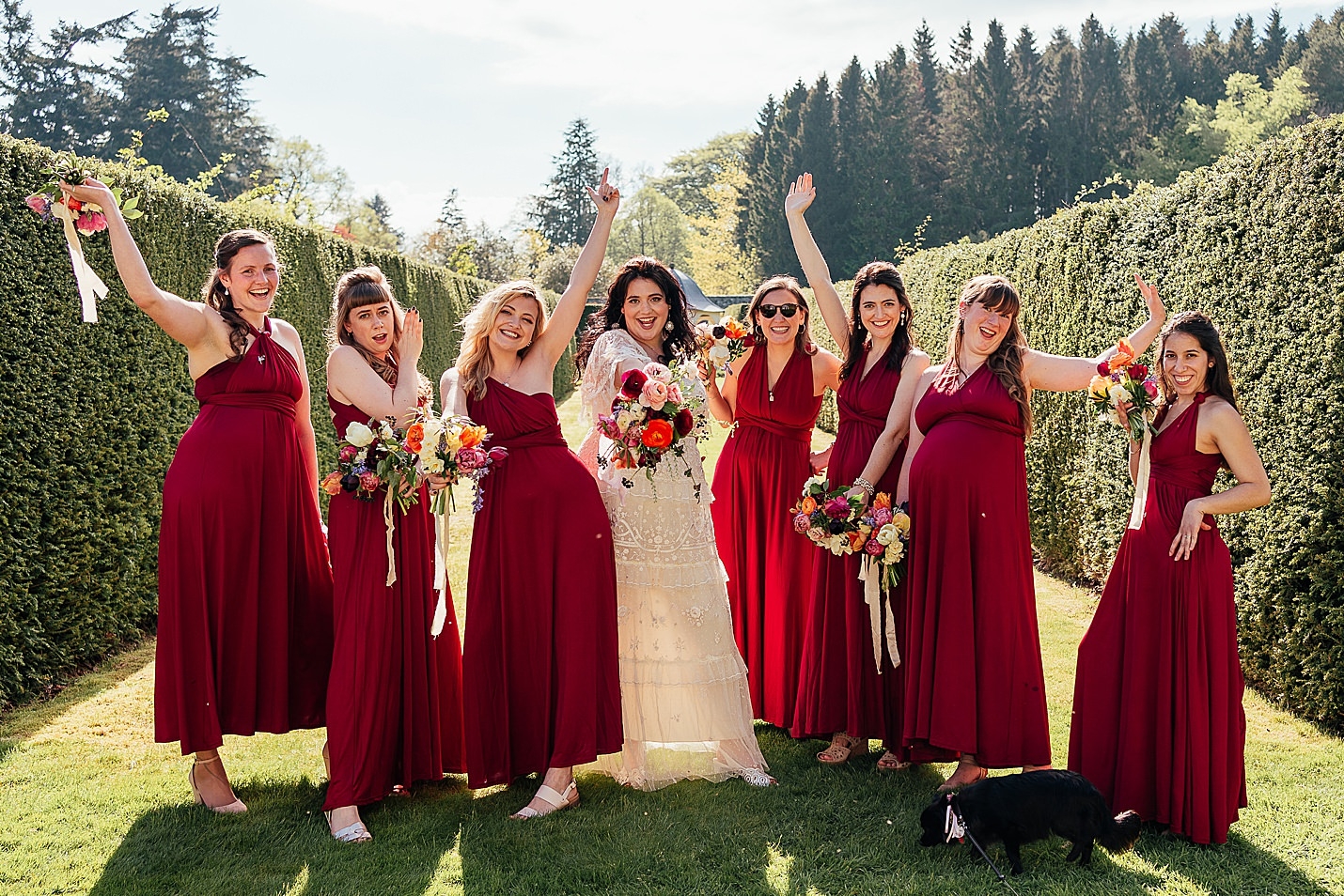 bride in white dress and seven bridemaids in red dresses posing for camera with hands in the air in walled garden drum castle wedding fotomaki photography