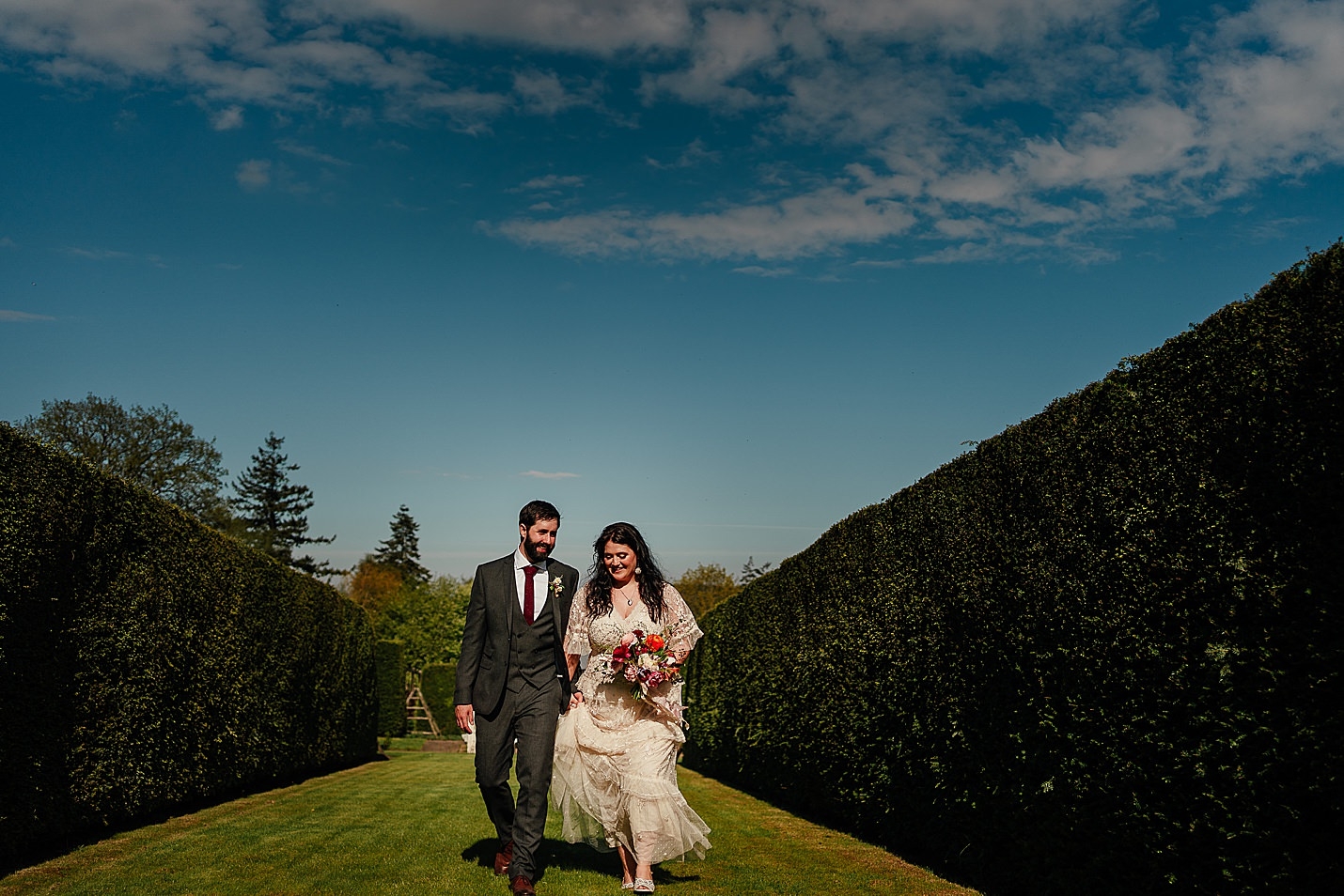 just married bride and groom walking towards camera in green walled garden with blue skies on sunny day drum castle wedding fotomaki photography